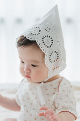 Side profile of baby in Avauma Clare Bonnet - Cotton Cream with eyelet embroidery and satin chin ribbon
